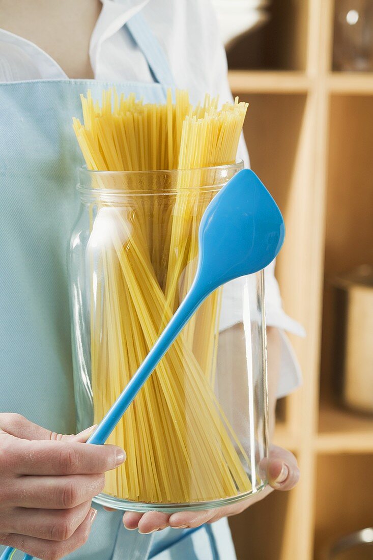 Frau hält Glas Spaghetti und Kochlöffel