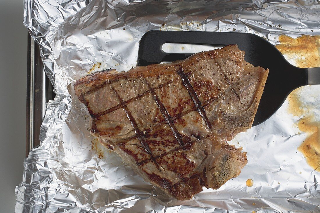 Grilled T-bone steak on aluminium foil with spatula