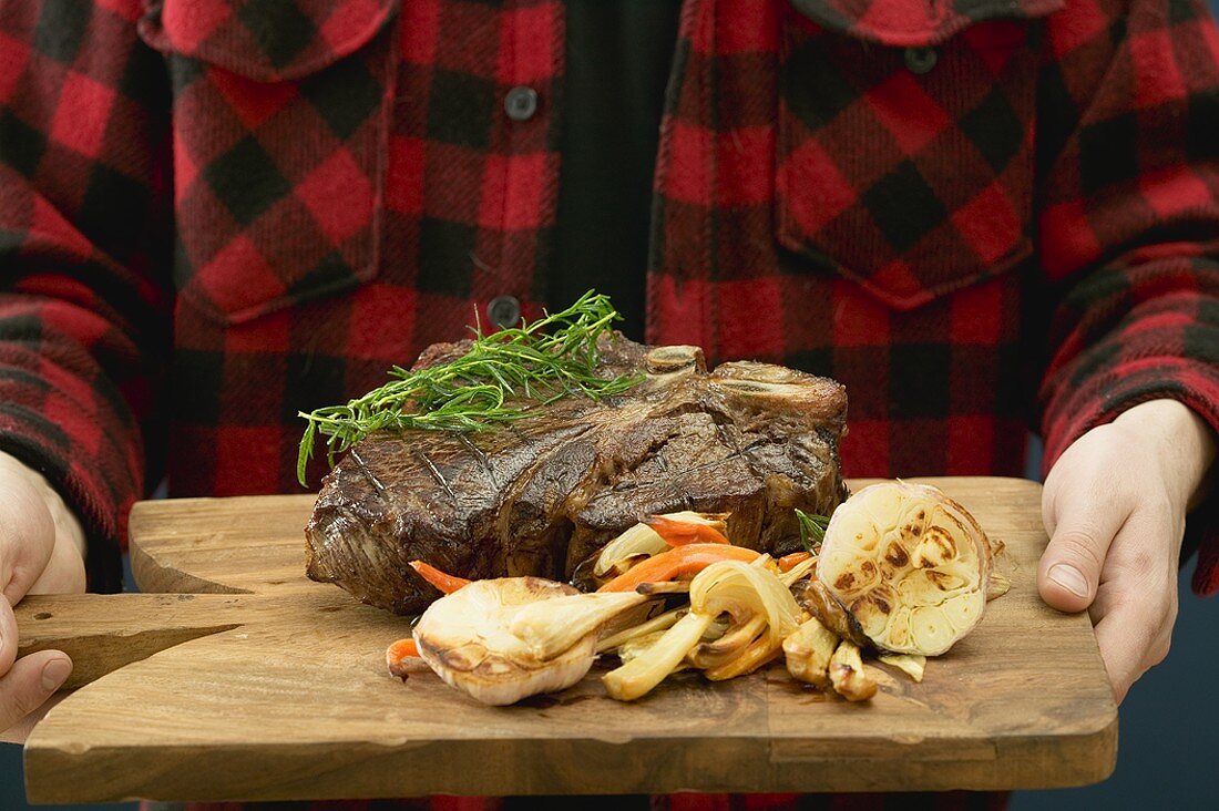 Mann serviert gegrilltes T-Bone-Steak auf Schneidebrett