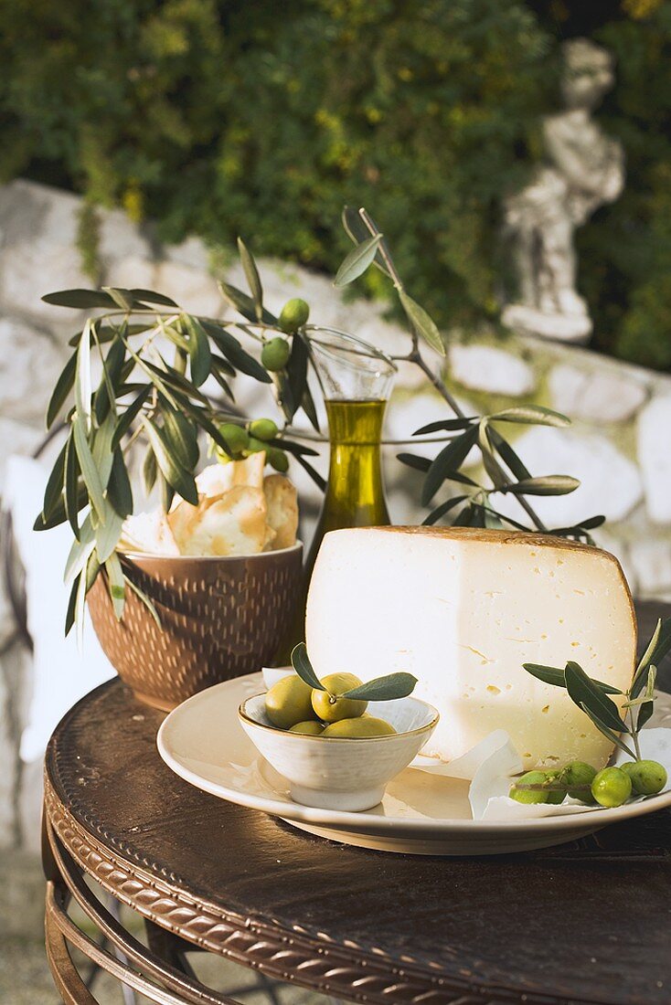 Olives, cheese, crackers & olive oil on table out of doors
