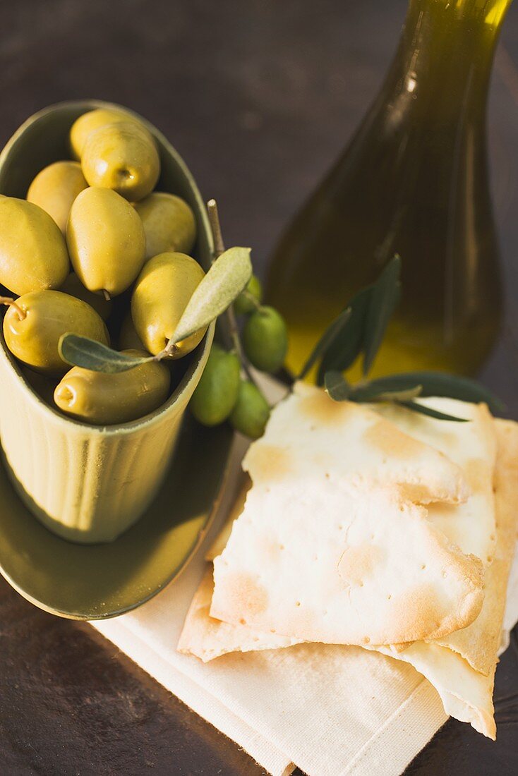 Grüne Oliven in Schale, daneben Cracker