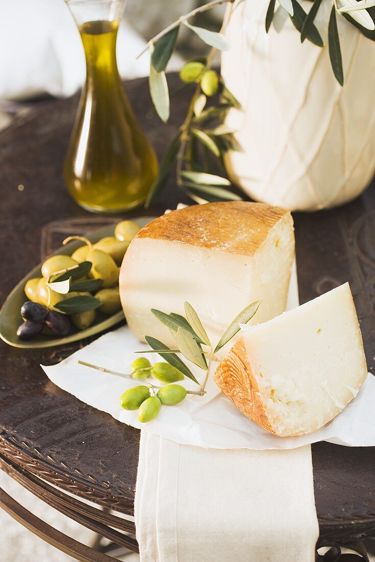 Cheese, olives and olive oil on table out of doors