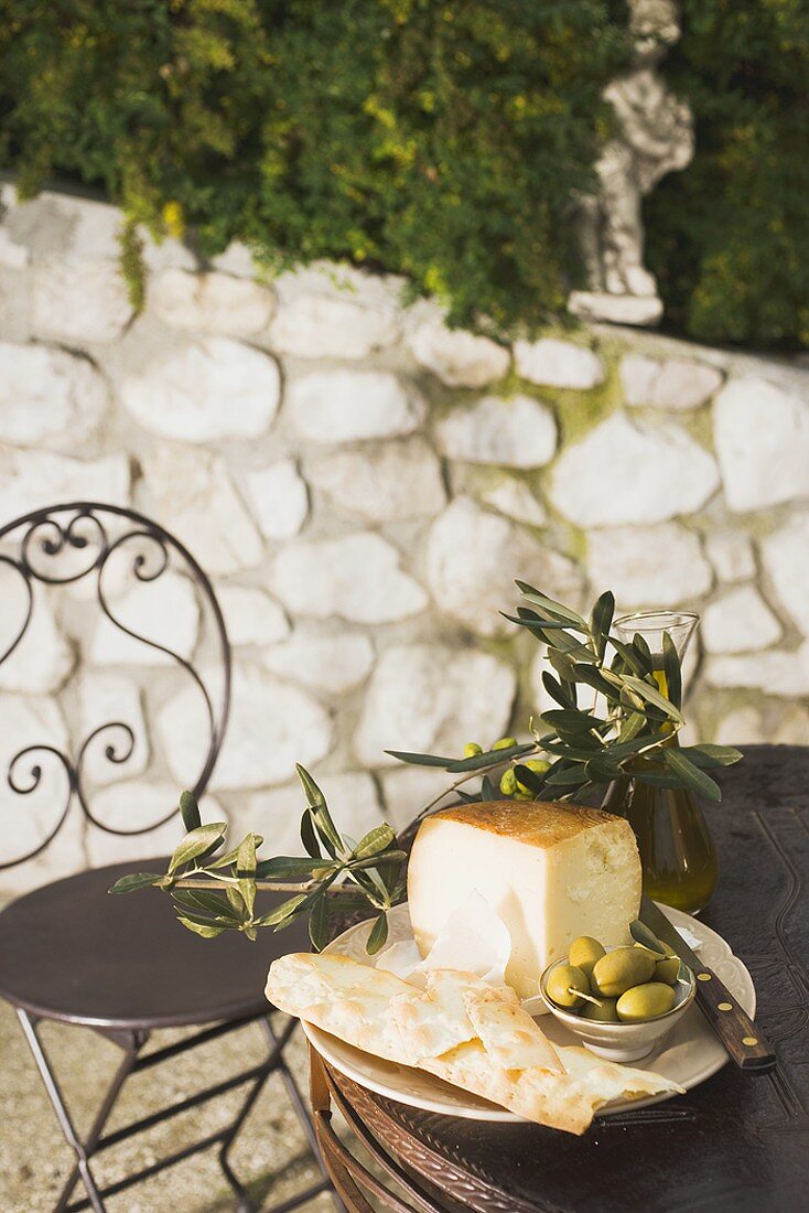 Käse, grüne Oliven, Cracker und Olivenöl auf Tisch im Freien