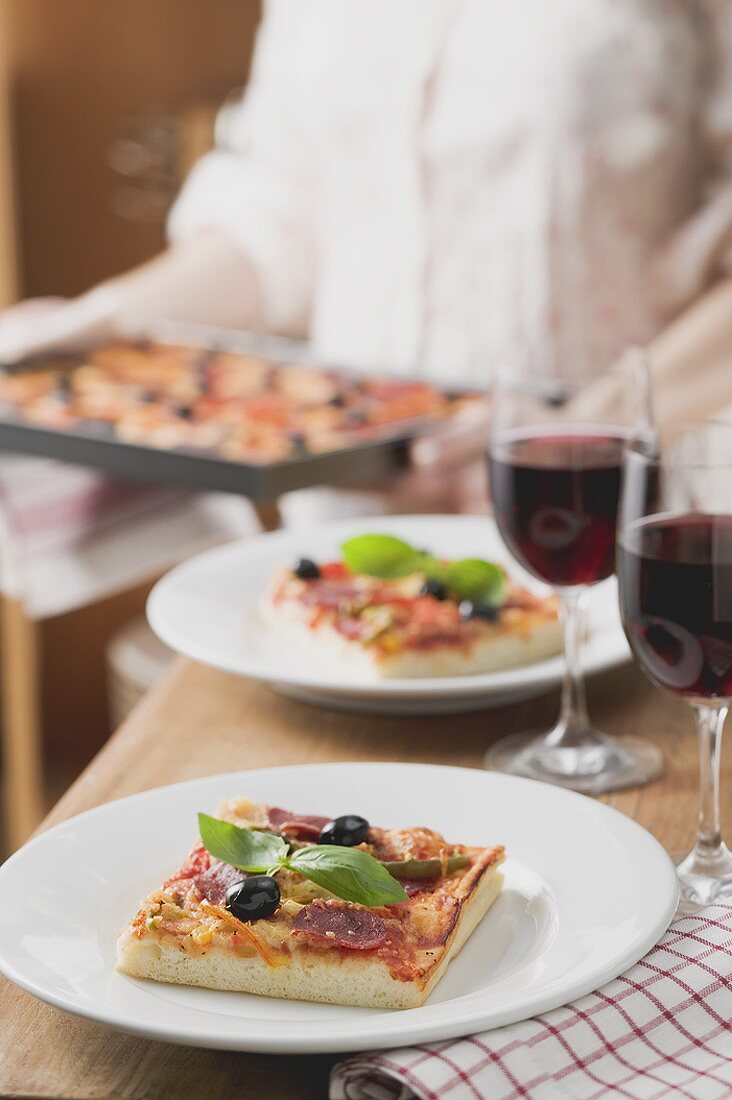 Slices of pepperoni pizza with olives, glasses of red wine