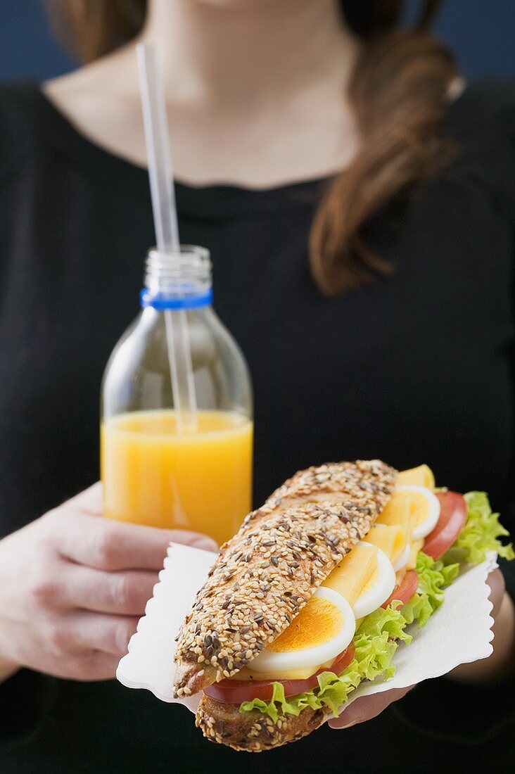 Frau hält Sandwich und Flasche Orangensaft
