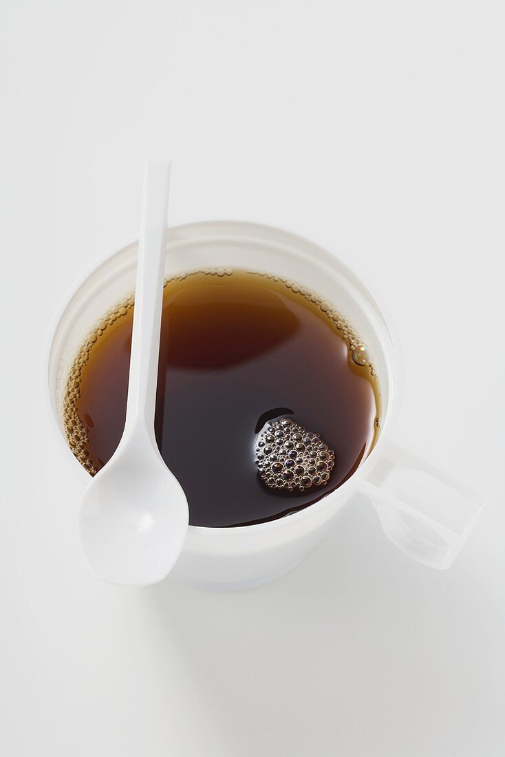 Schwarzer Kaffee im Plastikbecher mit Löffel darauf