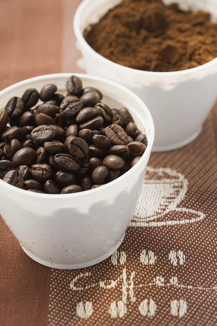 Kaffeebohnen und Kaffeepulver in zwei Bechern