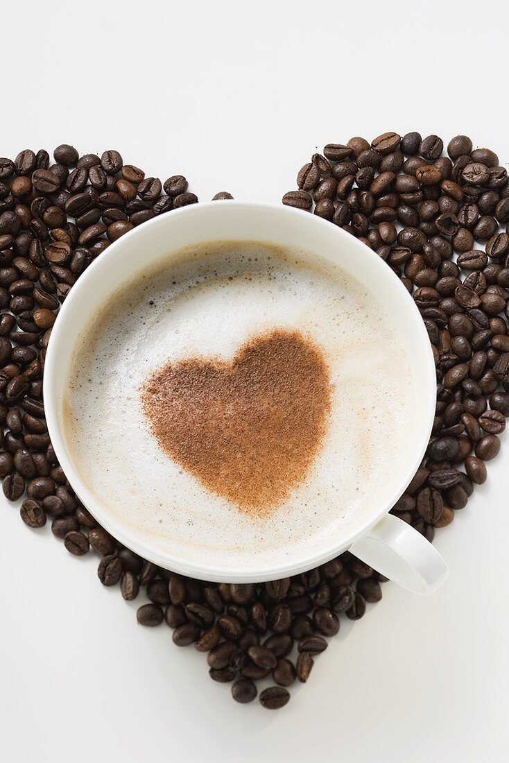 Tasse Cappuccino mit Kakaopulverherz auf Kaffeebohnen