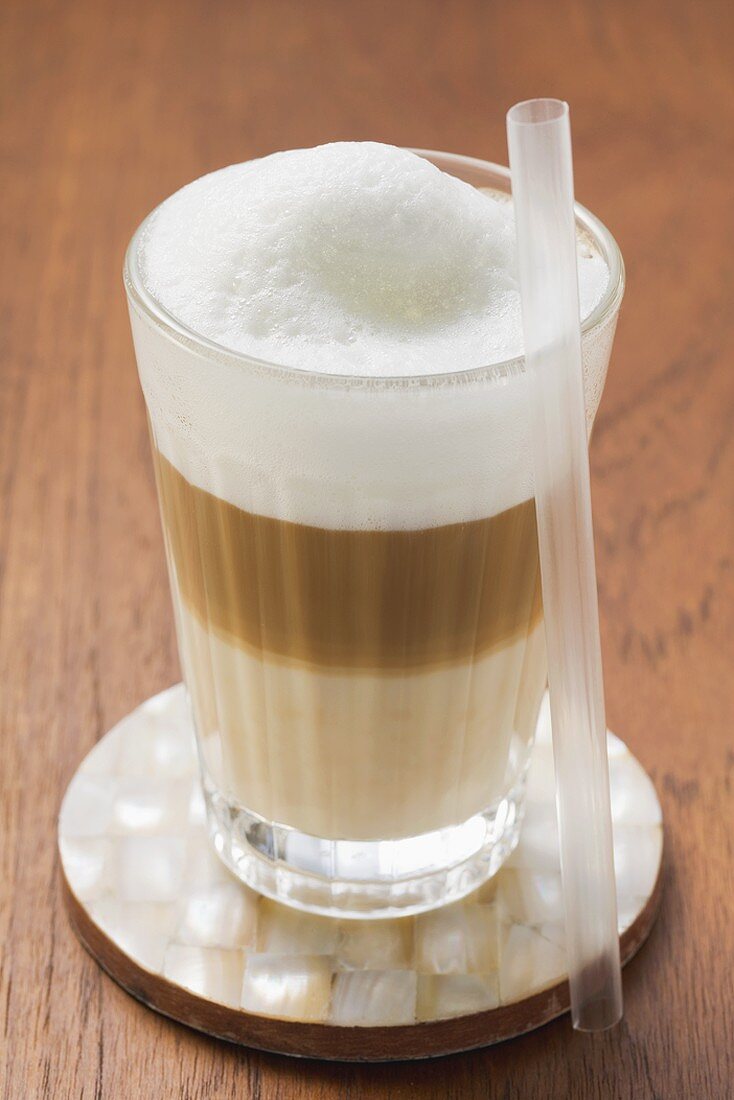 Latte Macchiato im Glas, daneben Strohhalm