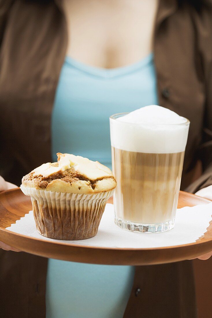 Frau hält Tablett mit Latte Macchiato und Muffin