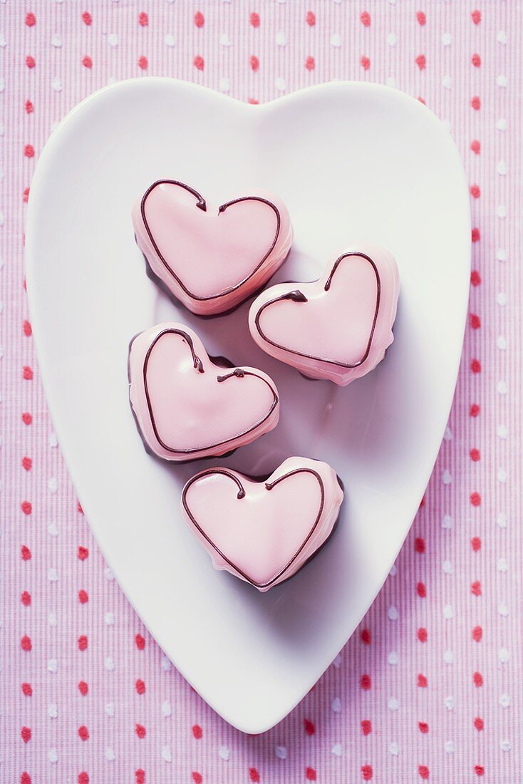 Vier herzförmige rosa Petit fours auf Teller