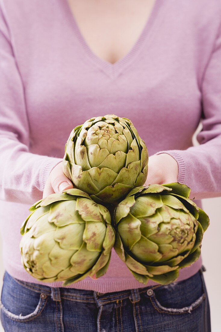 Woman holding three artichokes