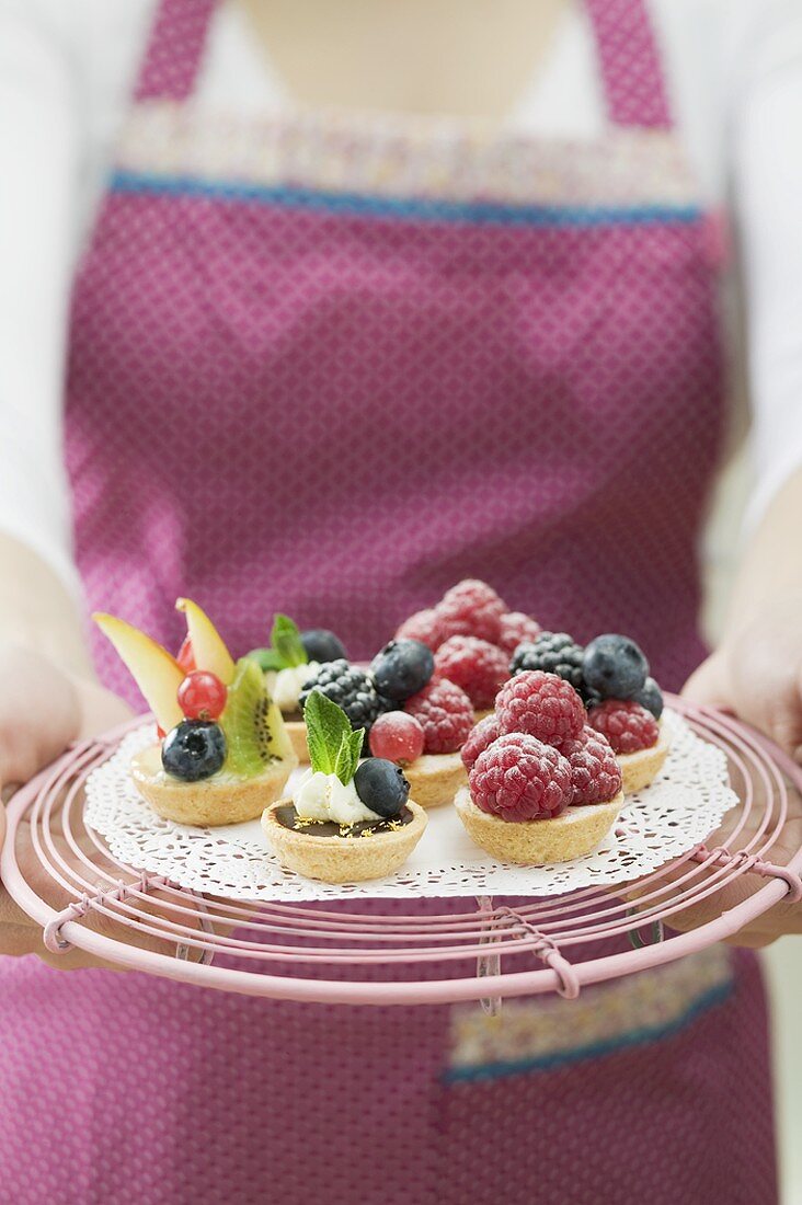 Woman in apron holding assorted berry tarts