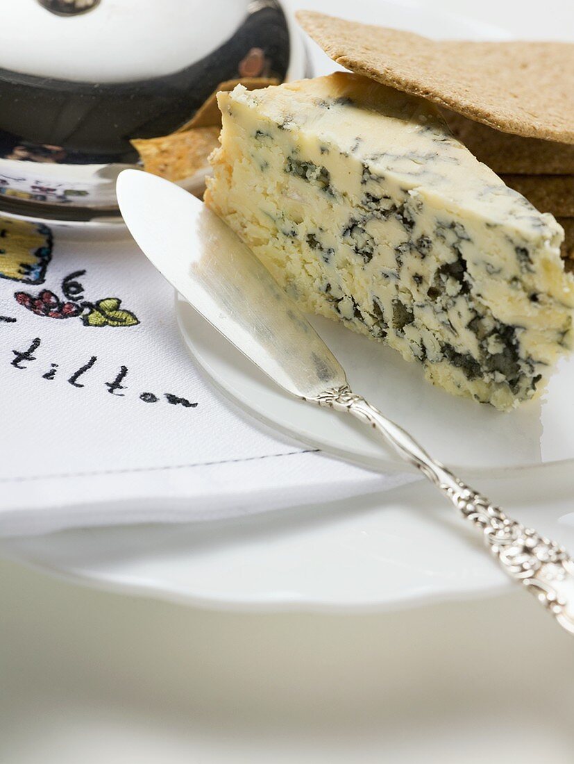 Stück Stilton mit Crackern und Käsemesser