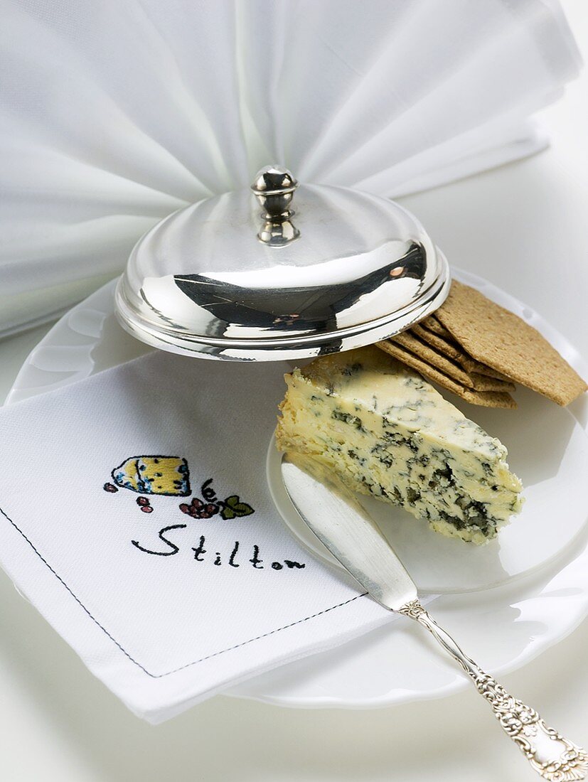 Stück Stilton mit Crackern und Käsemesser