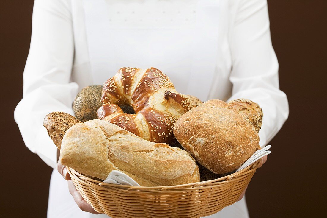 Chambermaid serving assorted bread rolls in bread basket