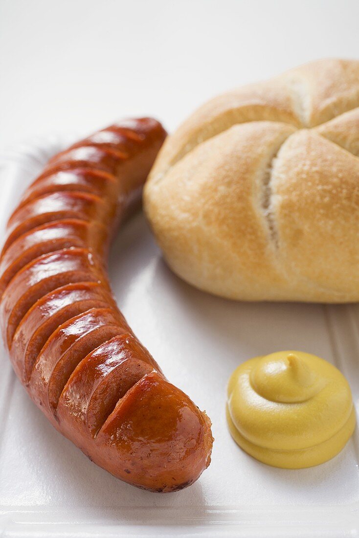 Sausage (bratwurst) with mustard & bread roll on paper plate