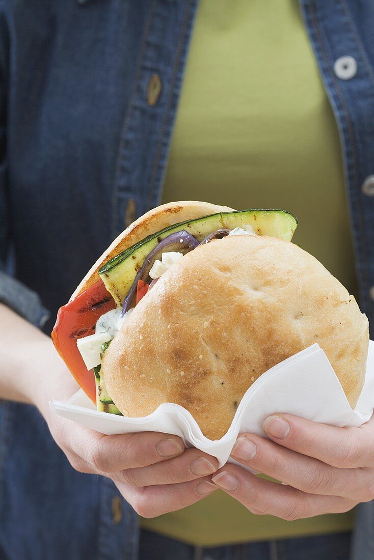 Woman holding toasted roll filled with grilled vegetables