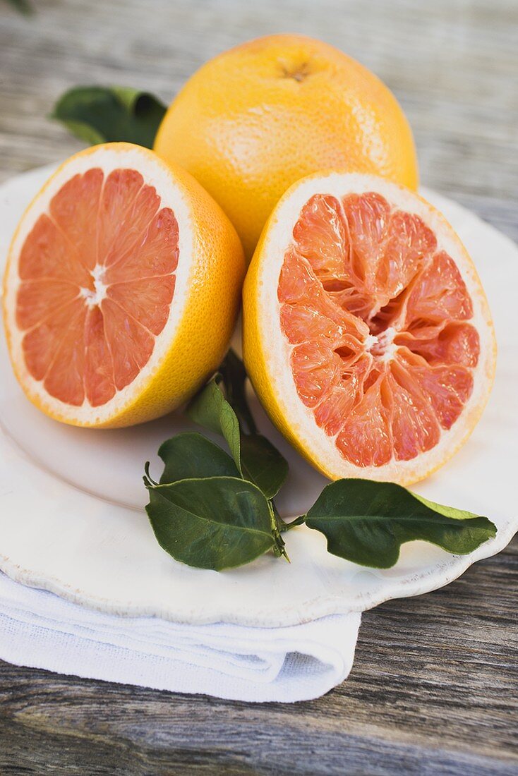 Rosa Grapefruits, ganz und halbiert, mit Blättern