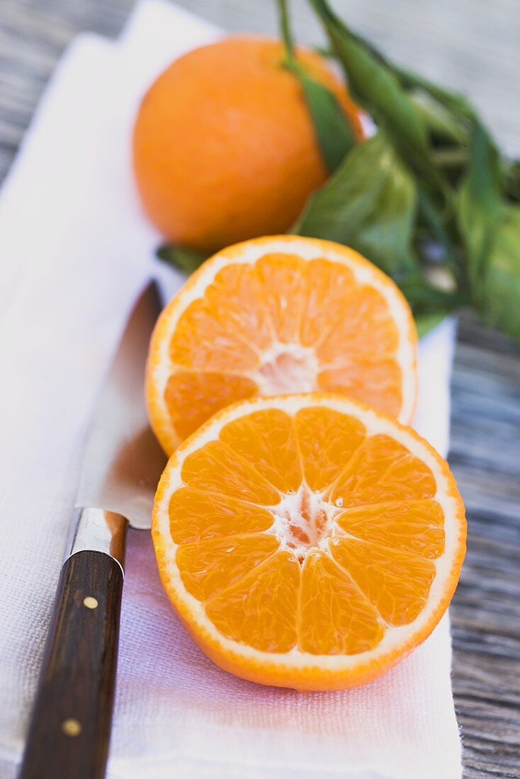 Clementinen, ganz und halbiert, auf weißem Tuch mit Messer