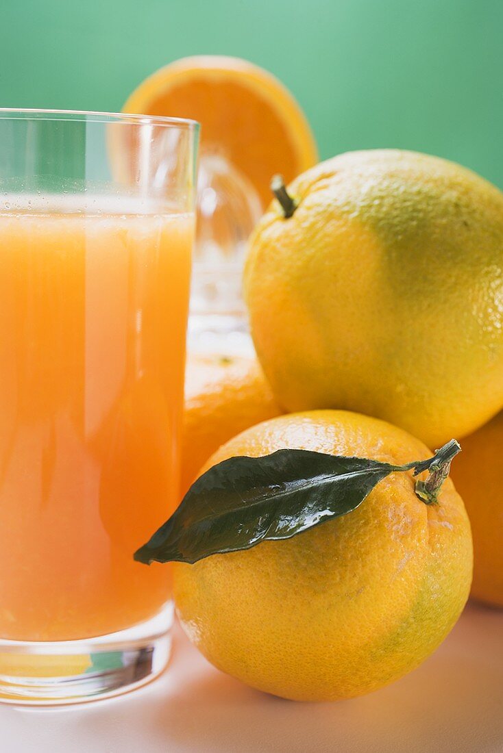 Glas Orangensaft, daneben mehrere Orangen