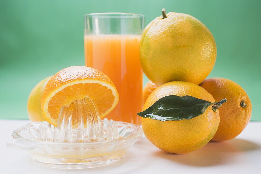 Glas Orangensaft, mehrere Orangen und Saftpresse