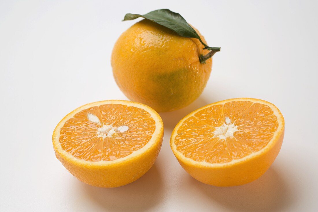 Two orange halves in front of whole orange with leaf