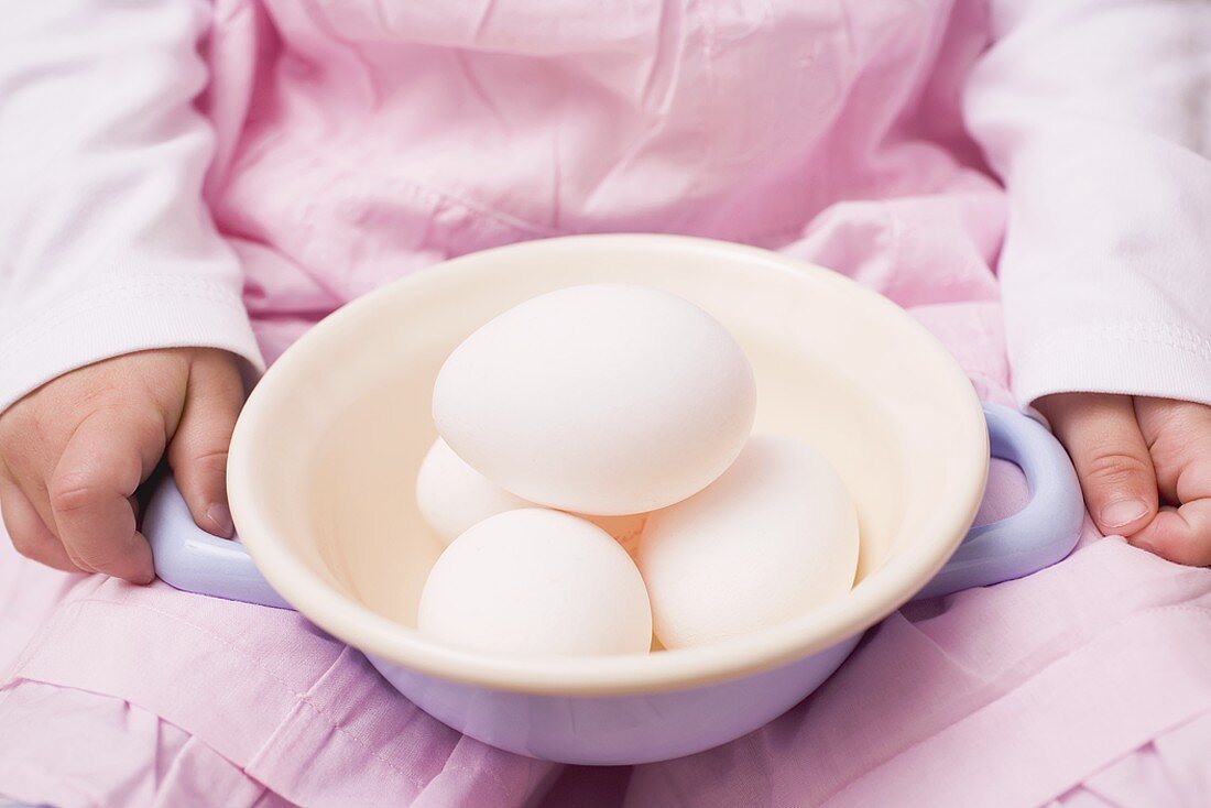 Child holding a dish of white eggs