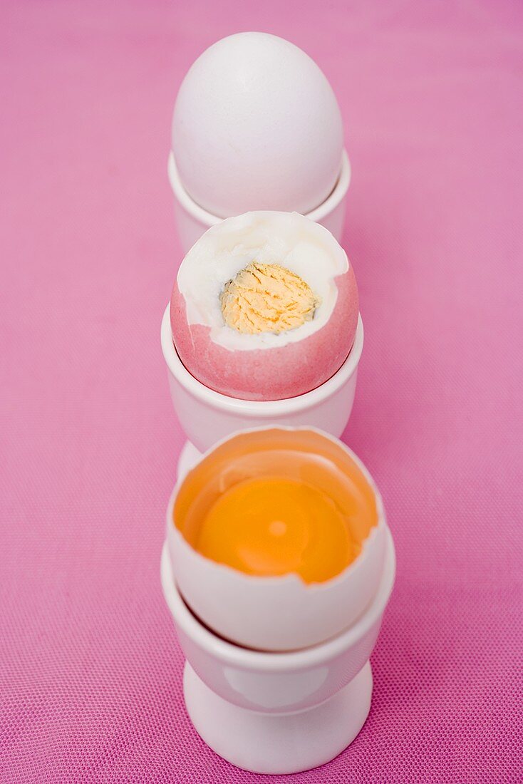 Three eggs in eggcups (raw & boiled with top cut off, whole)