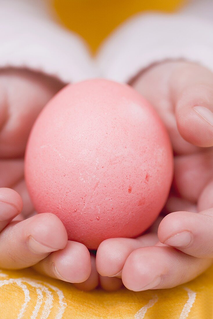Kinderhände halten rot gefärbtes Ei