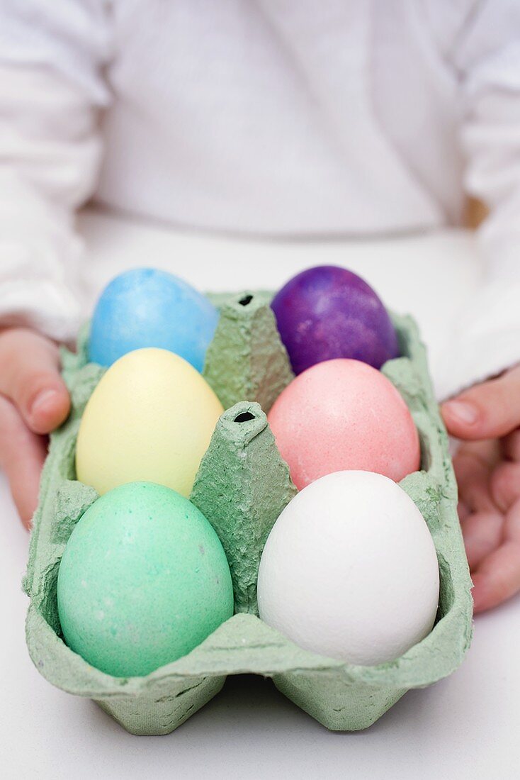 Kind hält Eierkarton mit gefärbten Eiern