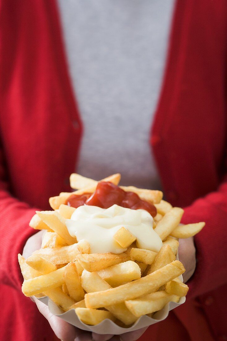 Woman holding paper dish of chips with ketchup & mayonnaise