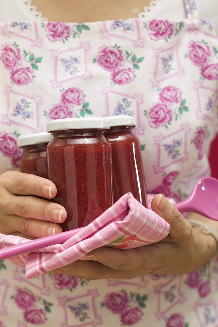 Woman holding jars of jam, tea towel and kitchen spoon