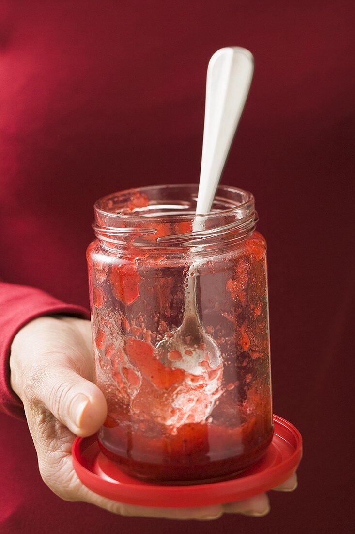 Frau hält Glas mit Resten von Erdbeermarmelade