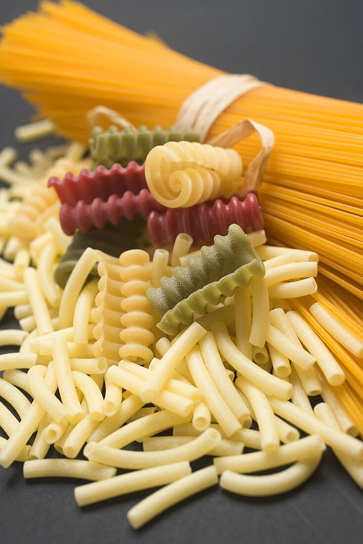 A bundle of spaghetti and various types of coloured pasta