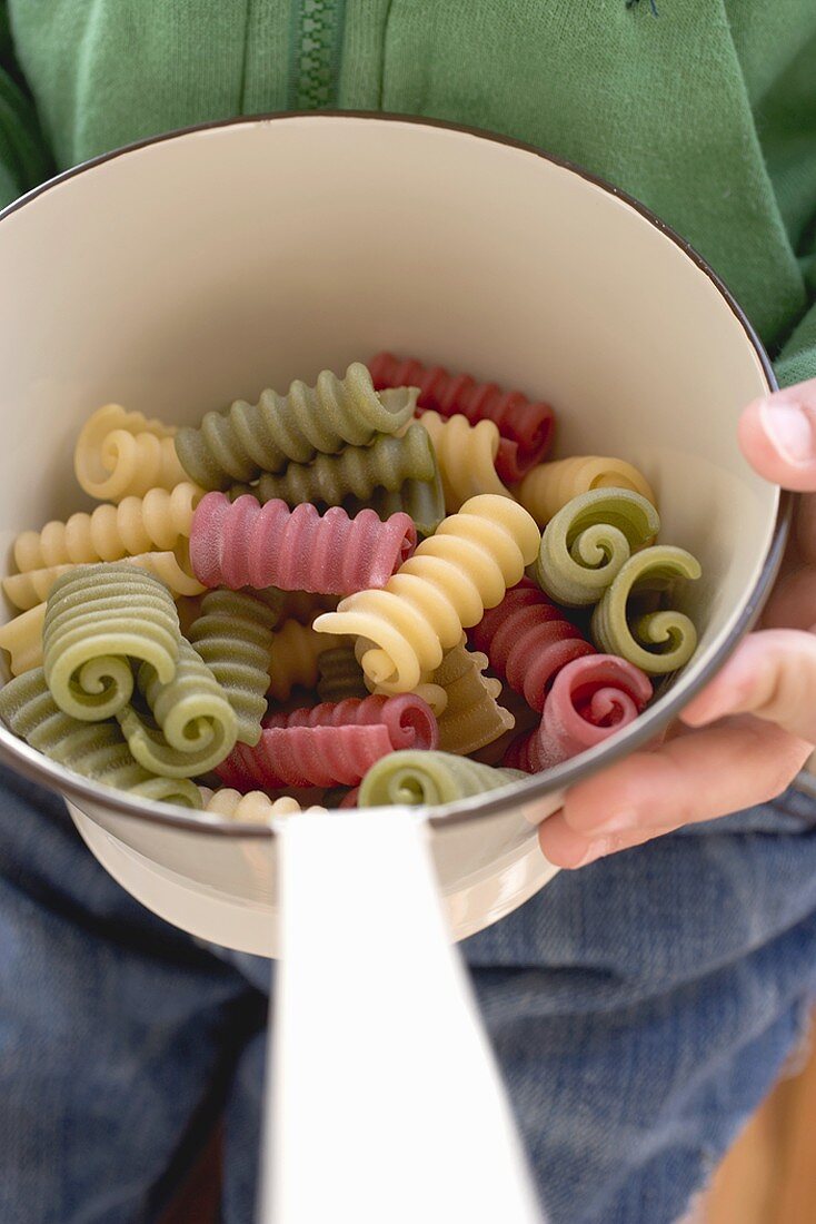Person holding strainer containing coloured pasta