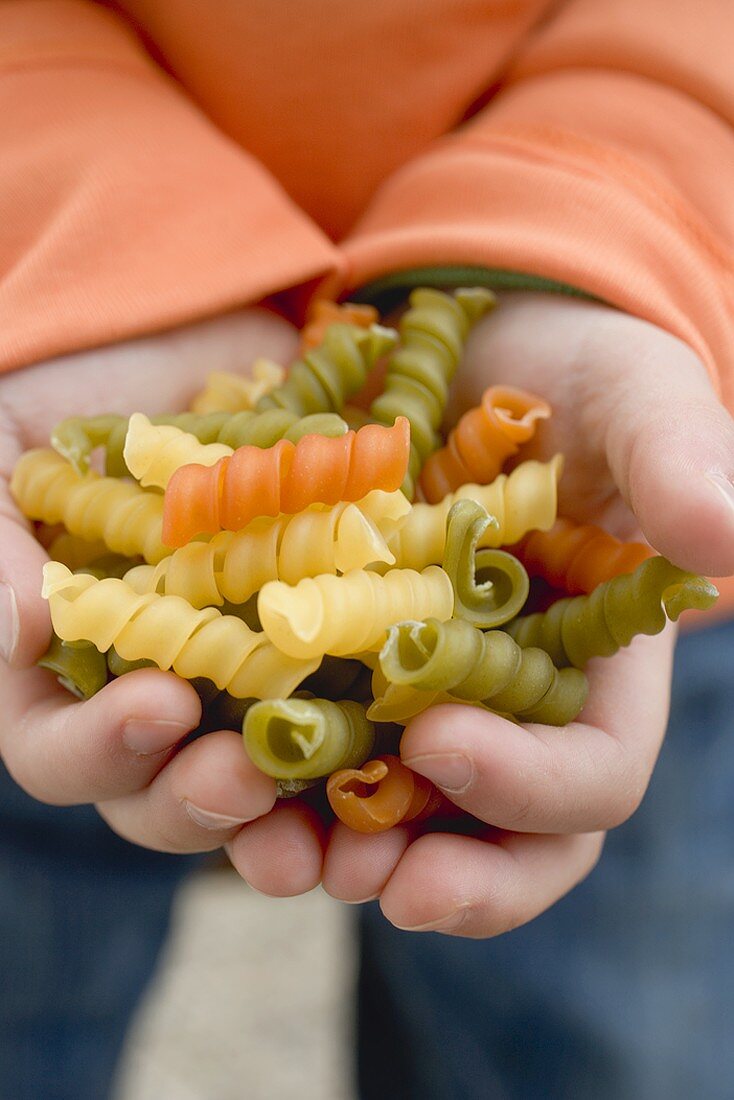 Child's hands holding coloured spiral pasta