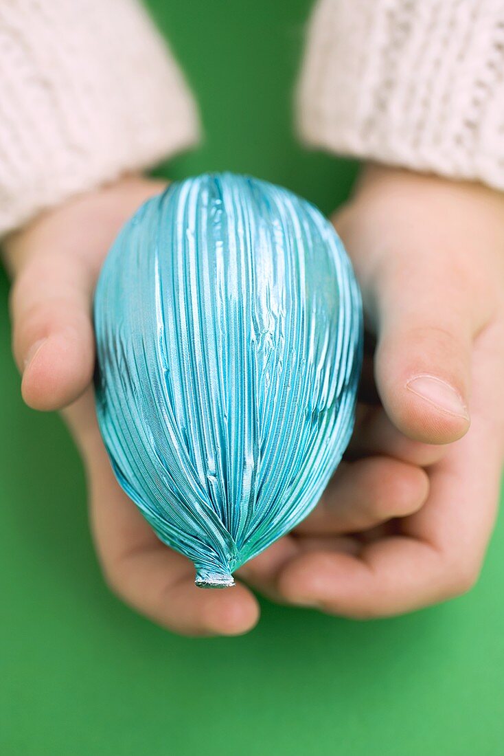 Child's hands holding Easter egg in blue foil
