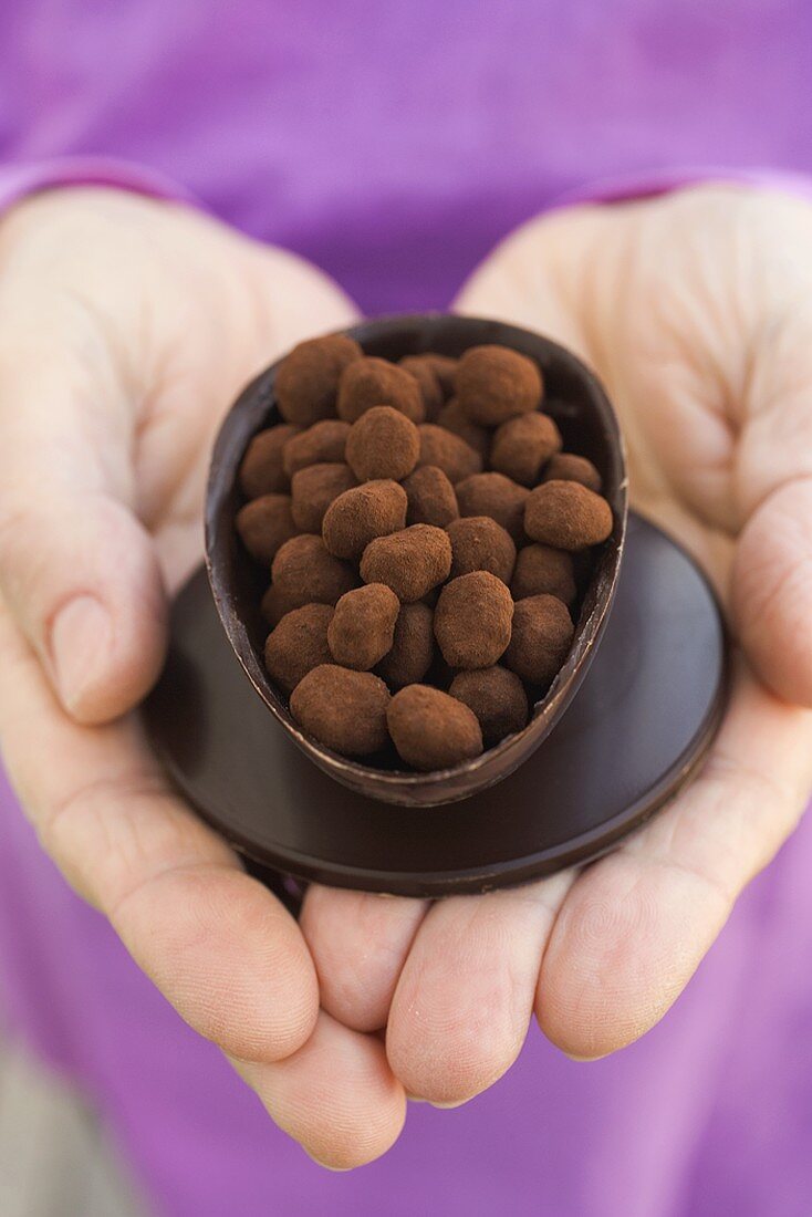 Hände halten halbes Schokoladenei, gefüllt mit Trüffeln