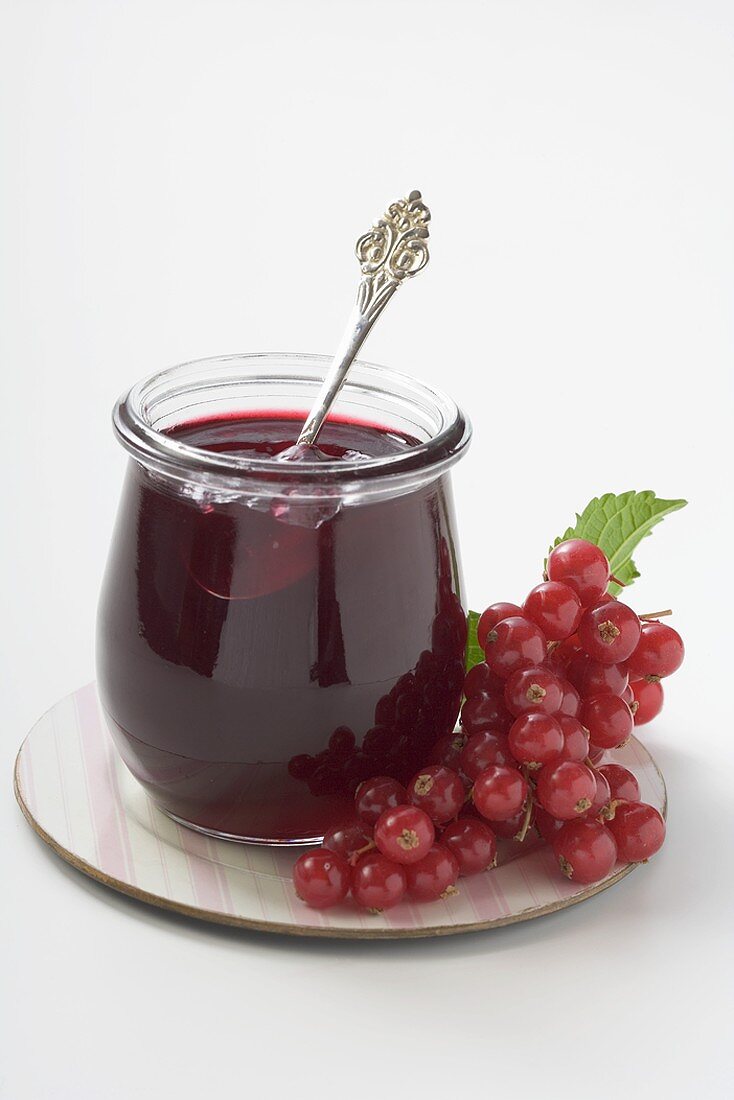 Glas Johannisbeergelee mit Löffel, daneben Johannisbeeren