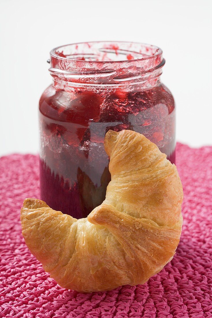 Jar of raspberry jam, croissant in foreground
