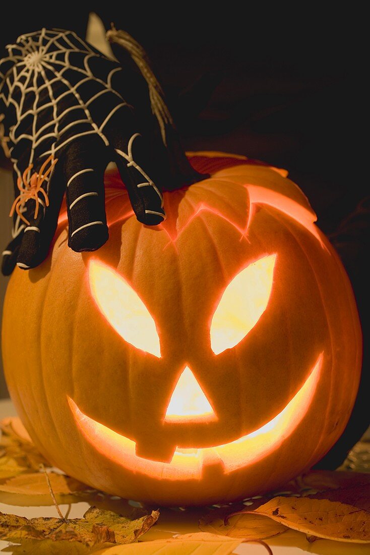 Hand in cobweb glove holding pumpkin lantern
