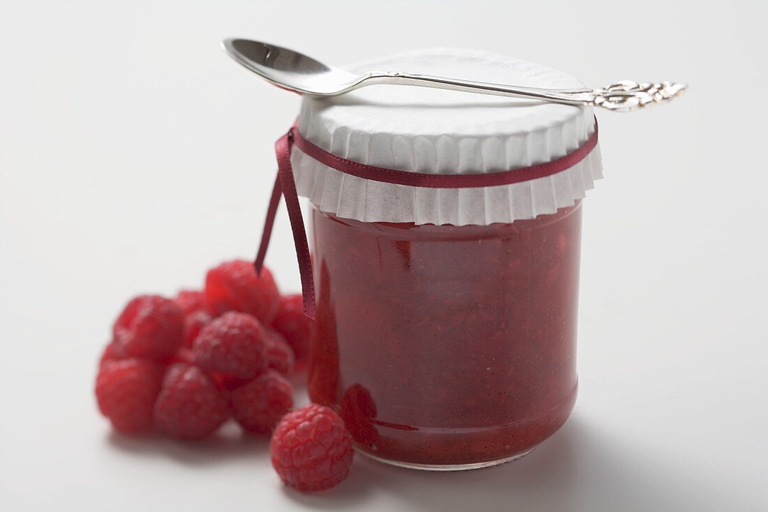 Jar of raspberry jam with spoon, fresh raspberries beside it