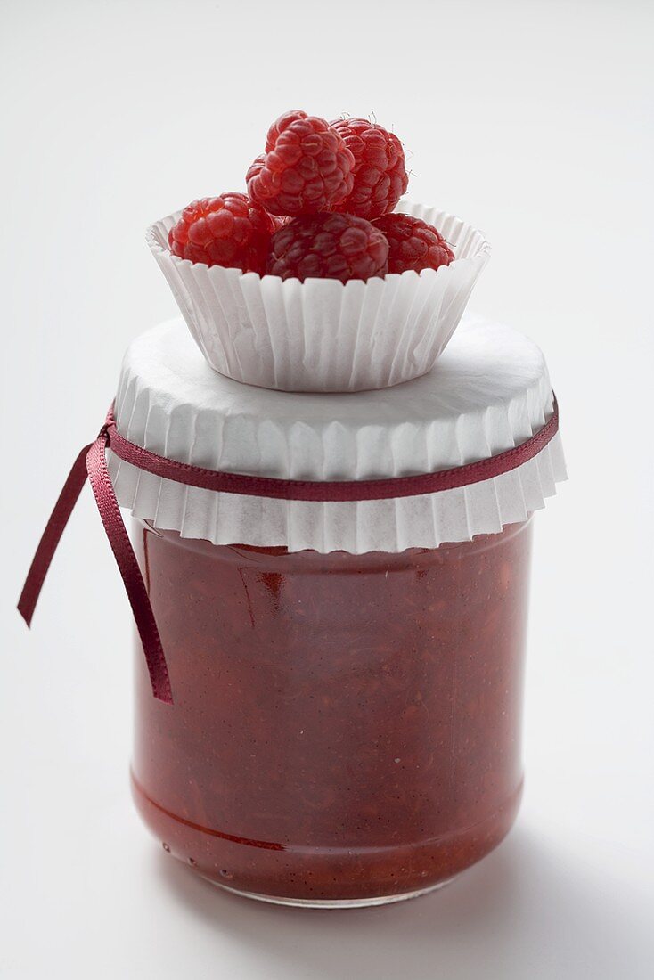 Jar of raspberry jam, raspberries in paper case on top