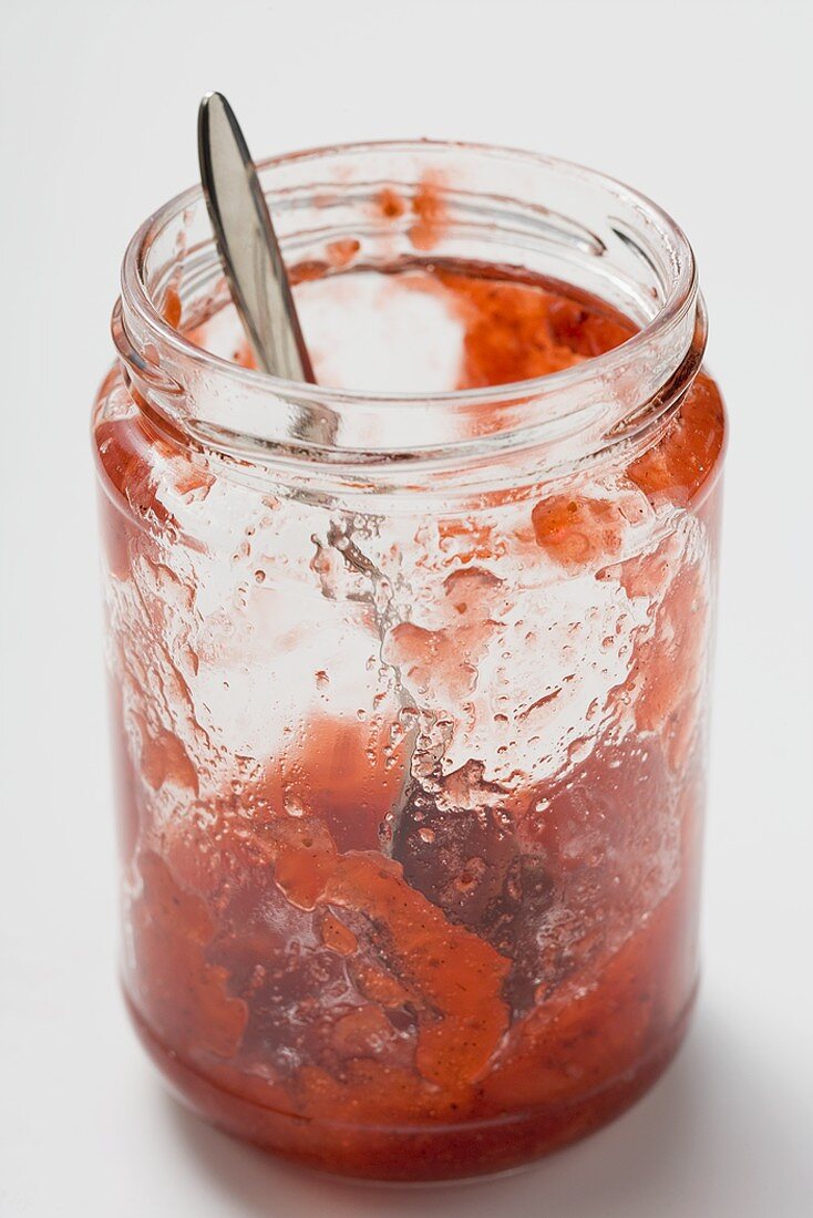 Marmeladenglas mit Löffel und Resten von Erdbeermarmelade