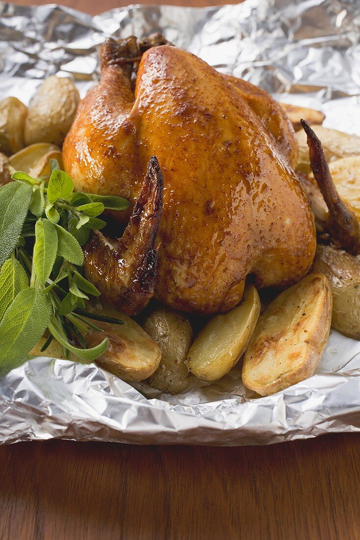 Roast chicken with potatoes and herbs on aluminium foil