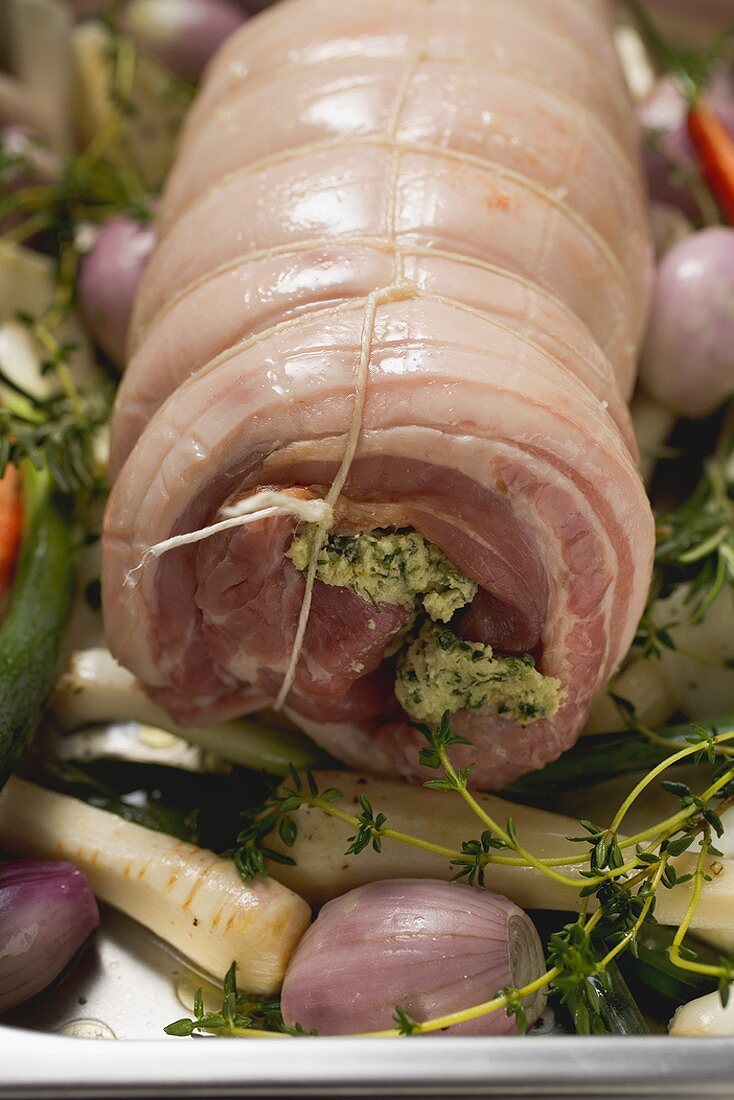 Raw rolled pork joint with vegetables on baking tray