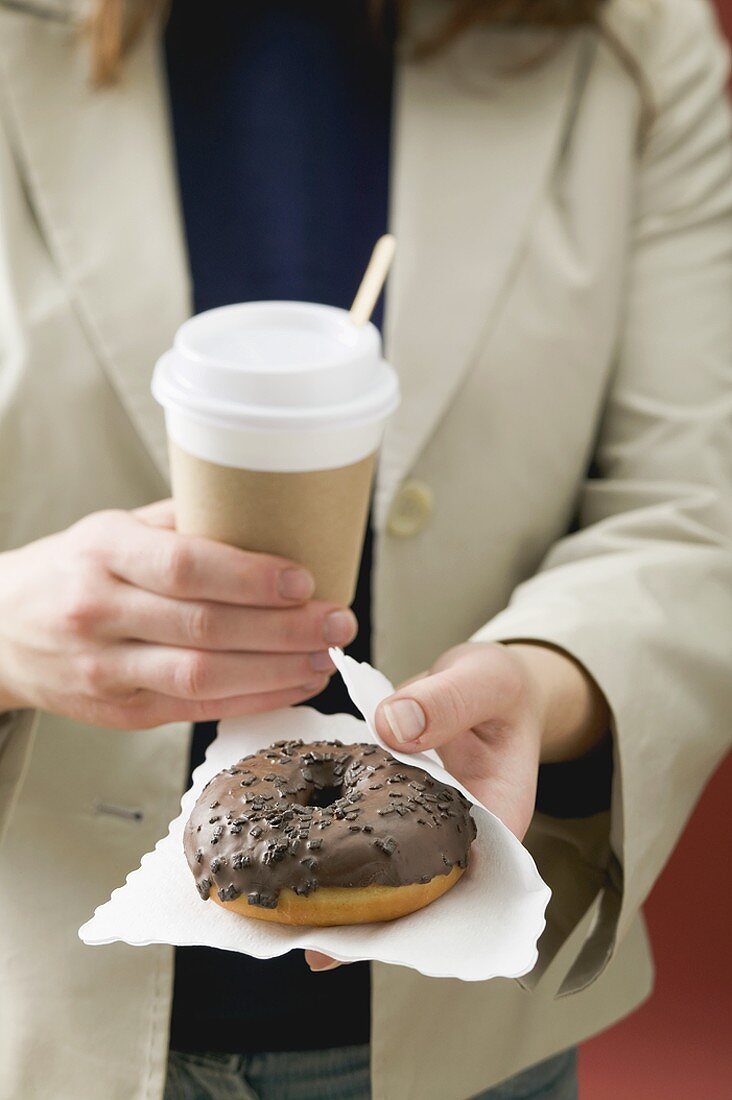 Woman holding chocolate doughnut and cup of coffee