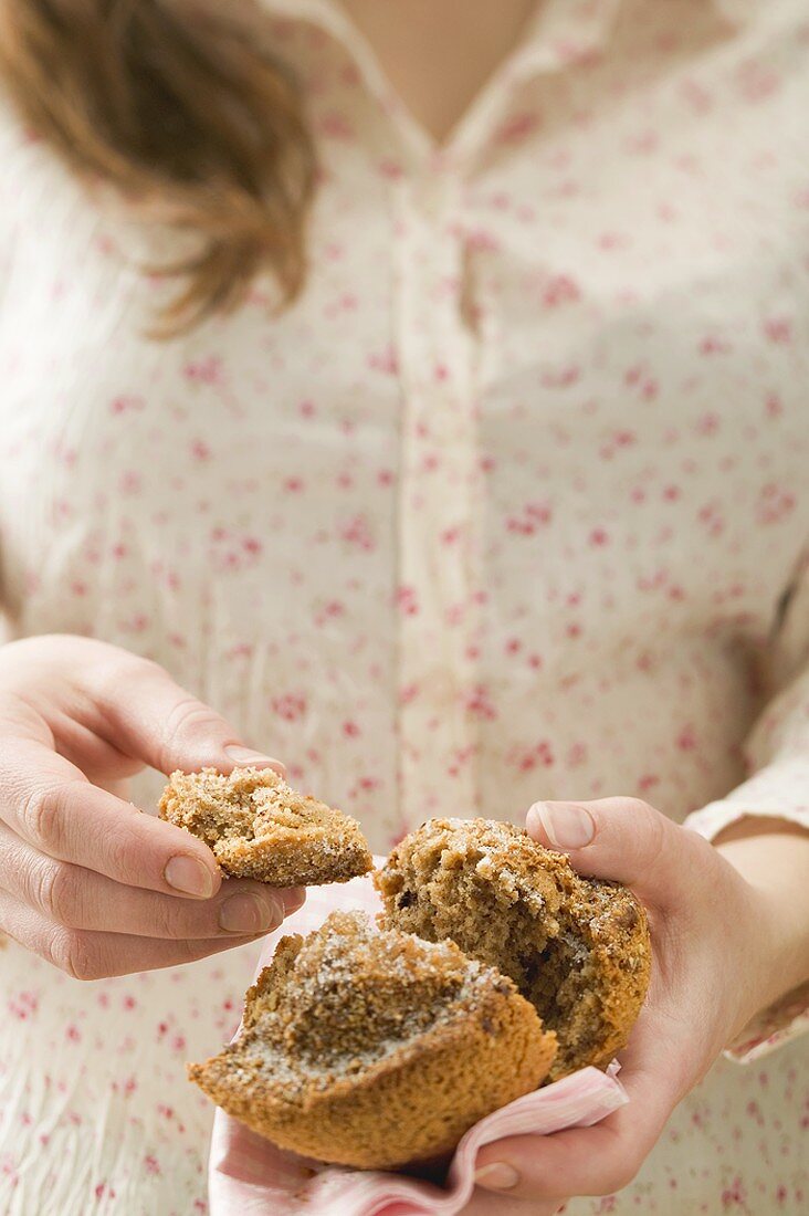 Frau hält halbiertes Muffin auf karierter Serviette