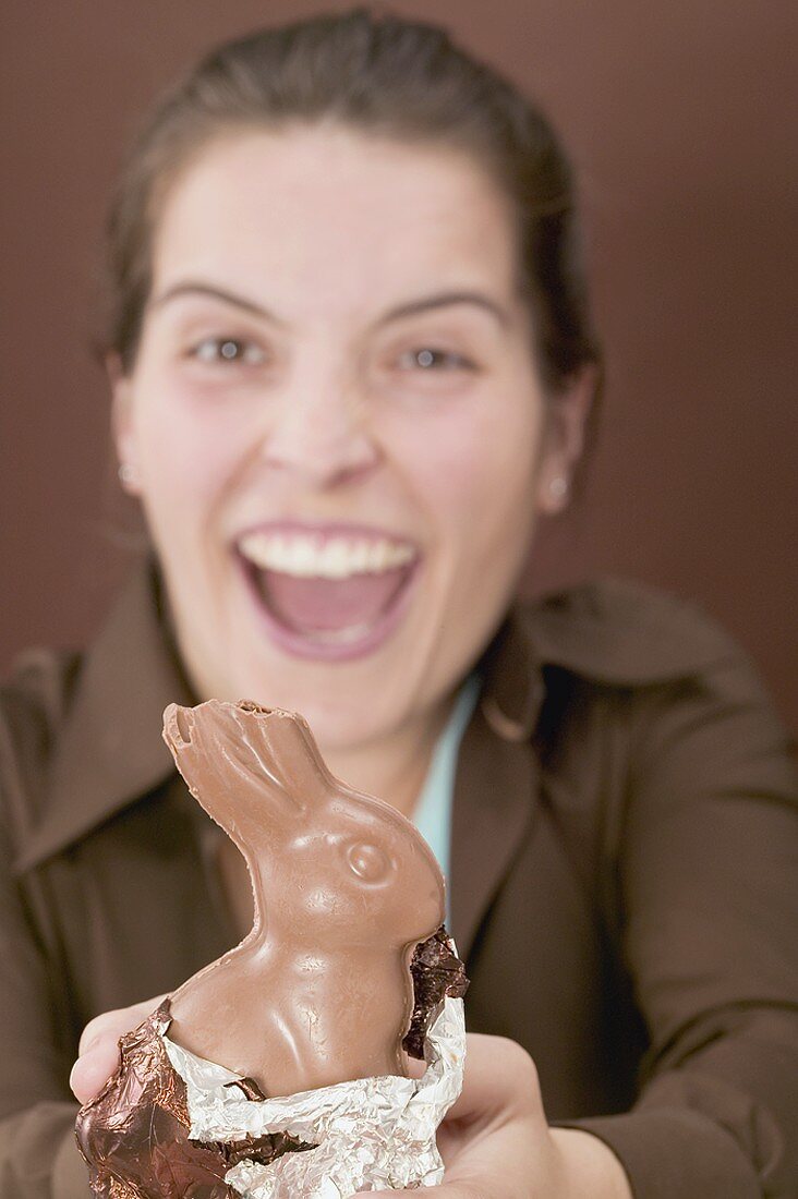 Lachende Frau hält angebissenen Schokoladenosterhasen